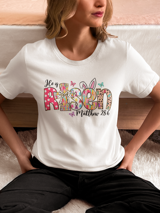 He Is Risen Easter tee with bunny ears design on a white shirt.