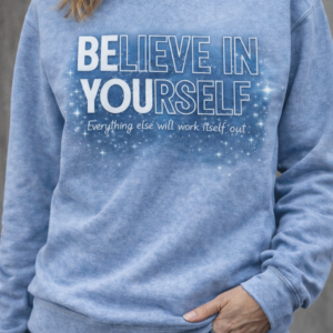 Woman wearing a light blue sweatshirt with the phrase “Believe in Yourself” and a starry motivational design.