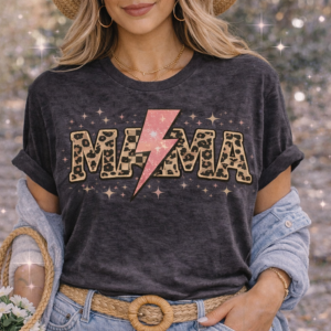 Woman wearing a dark charcoal vintage style t-shirt featuring the word MAMA in leopard print letters with a pink lightning bolt replacing the center letter, surrounded by sparkles for a trendy western glam look.